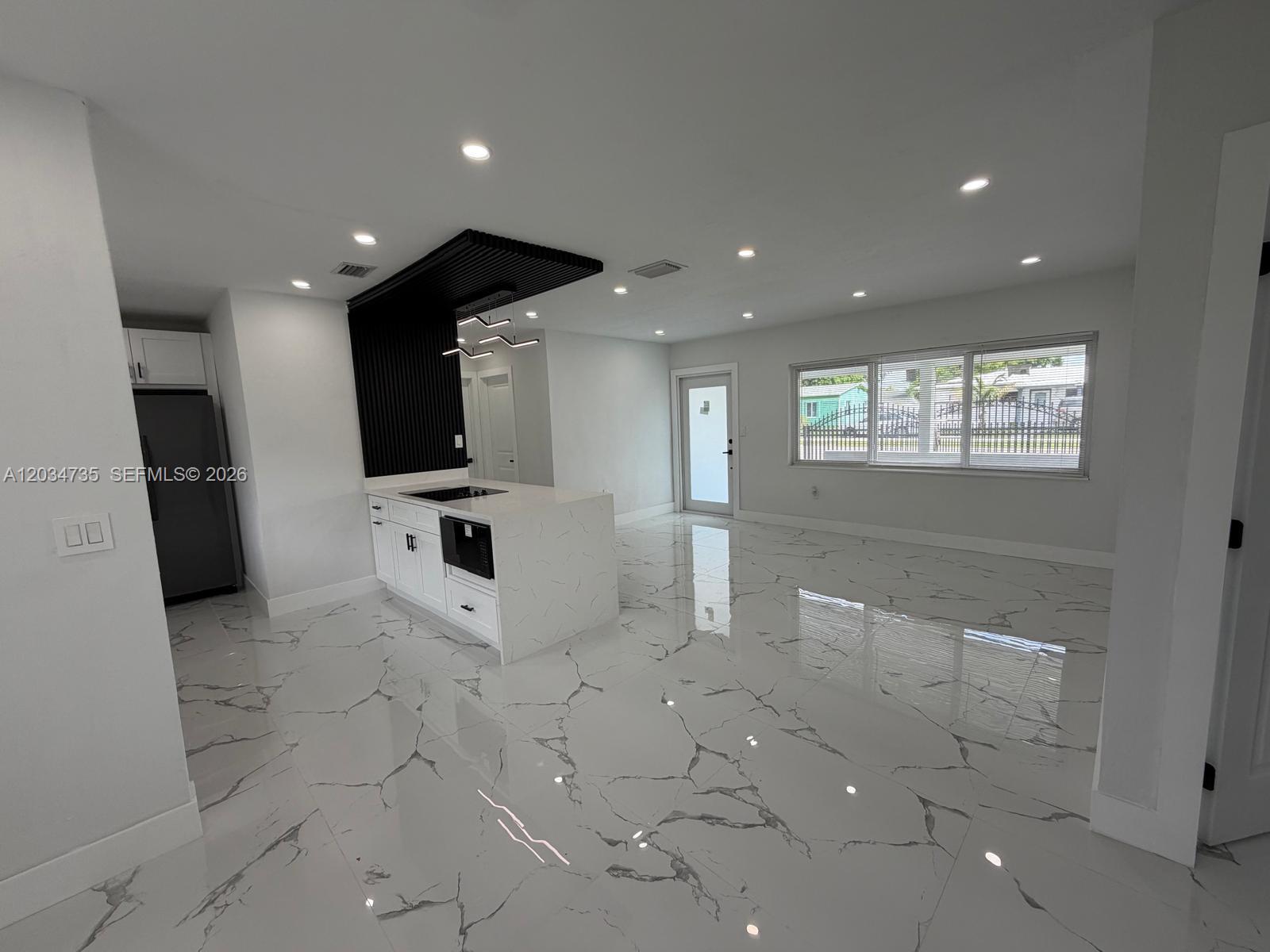 A modern kitchen features a white marble island, black slat ceiling detail, and polished flooring — 2800 NW 164th St, Miami Gardens FL 33054, MIAMI GARDENS, FL