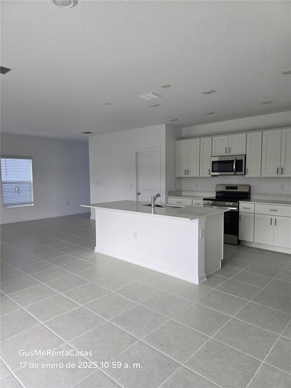 A modern kitchen features white cabinetry, a central island, and light-colored tile flooring — 5794 LE MARIN WAY, KISSIMMEE, FL