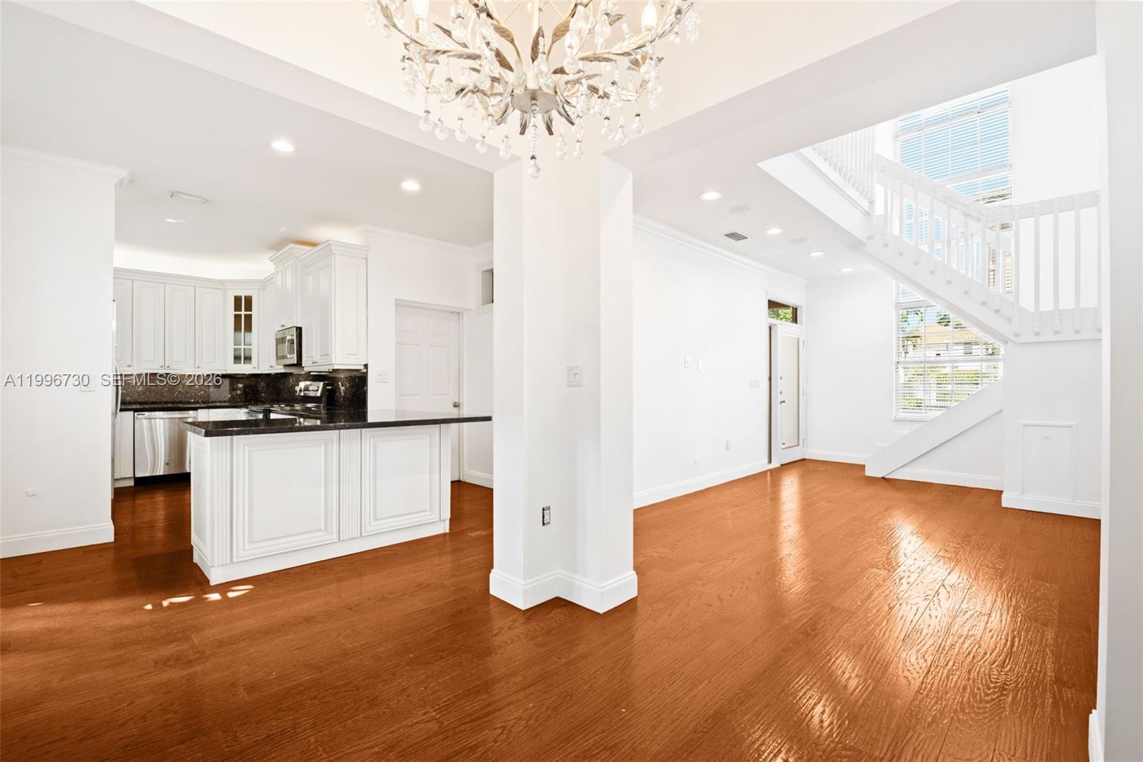 A kitchen with white cabinets and dark countertops opens to a living area with stairs — 3135 Gifford Ln # C, Miami FL 33133, MIAMI, FL