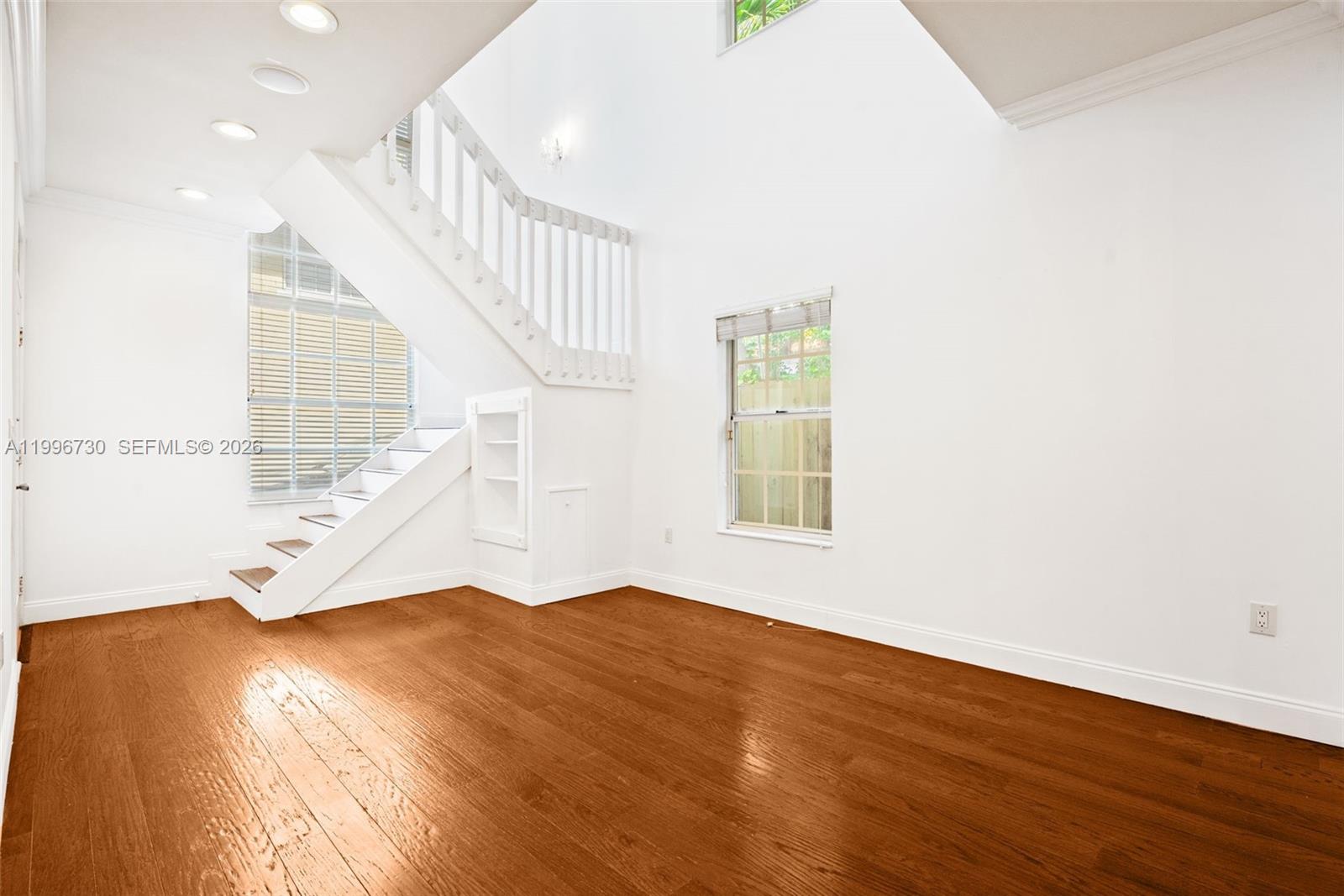 A room with hardwood floors, a white staircase, and a window under a vaulted ceiling — 3135 Gifford Ln # C, Miami FL 33133, MIAMI, FL