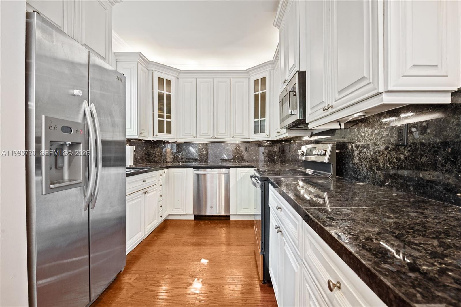A kitchen features white cabinets, dark granite countertops, stainless steel appliances, and hardwood flooring — 3135 Gifford Ln # C, Miami FL 33133, MIAMI, FL