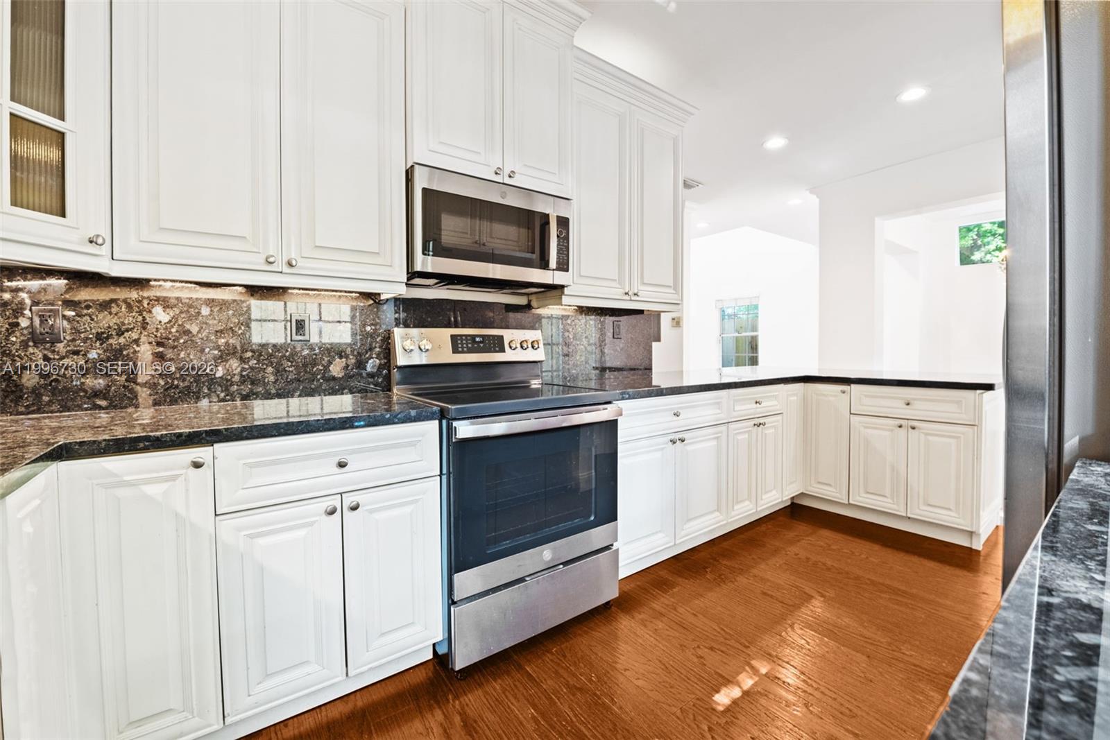 A kitchen features white cabinetry, dark granite countertops, stainless steel appliances, and hardwood flooring — 3135 Gifford Ln # C, Miami FL 33133, MIAMI, FL