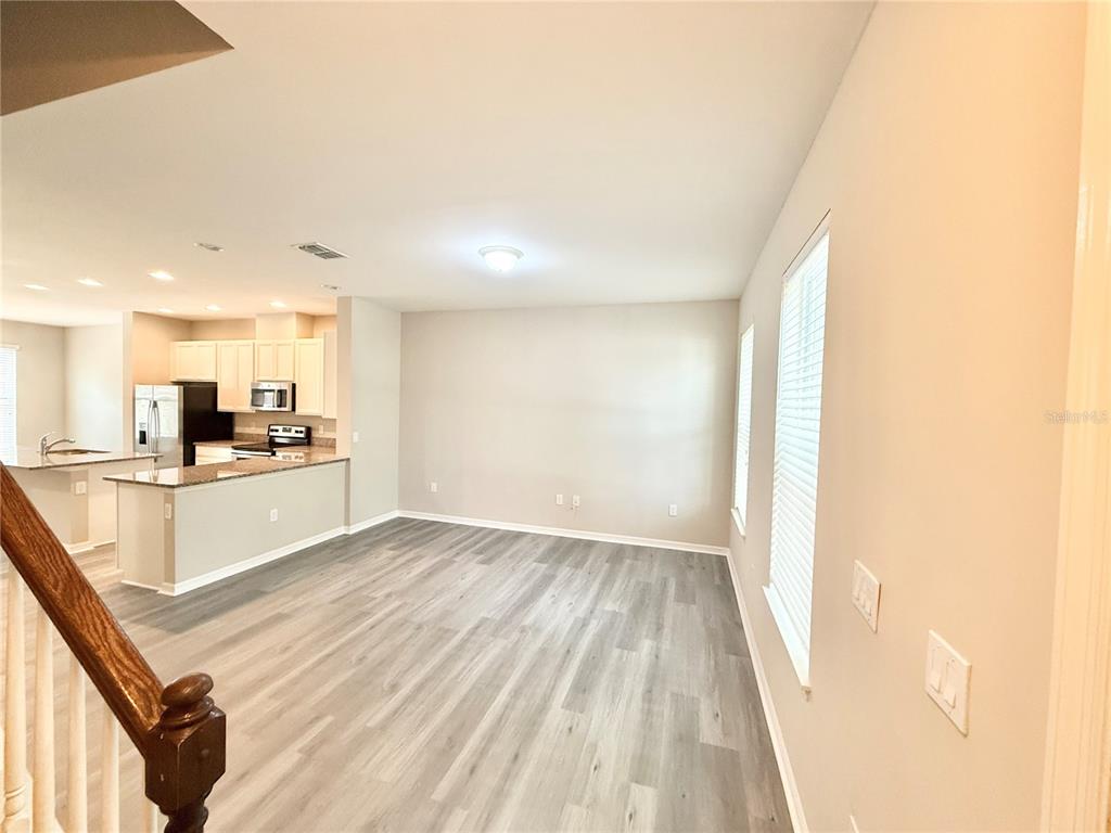 An open-concept living area features light wood-look flooring, neutral walls, and an adjacent kitchen — 11686 WATER RUN ALLEY, WINDERMERE, FL