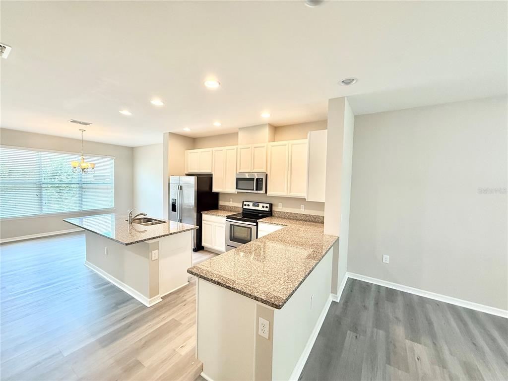 A kitchen features white cabinets, granite countertops, stainless steel appliances, and light wood-look flooring — 11686 WATER RUN ALLEY, WINDERMERE, FL