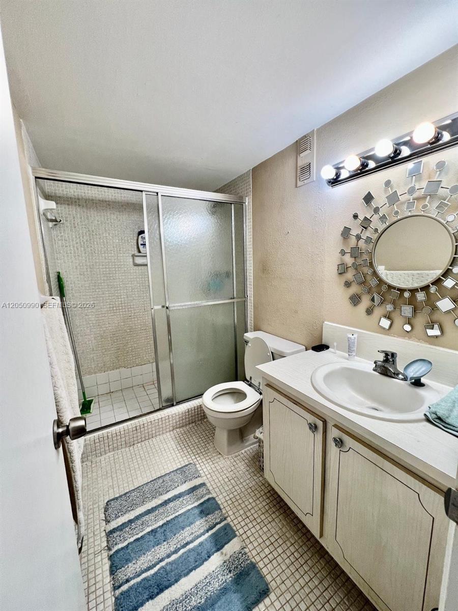 A bathroom features a tiled shower, a toilet, and a vanity with a decorative mirror — 1700 NE 191st St # 508, Miami FL 33179, MIAMI, FL