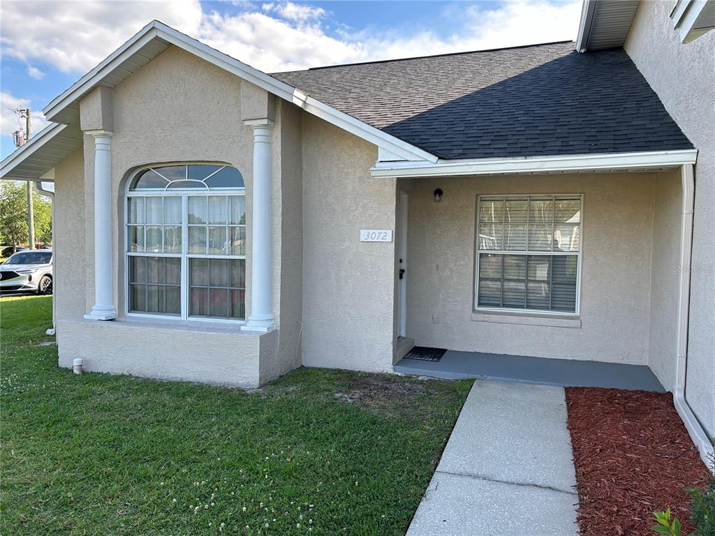 The exterior of a beige stucco house features a front porch, columns, and two windows — 3072 SHINGLE CREEK COURT, KISSIMMEE, FL