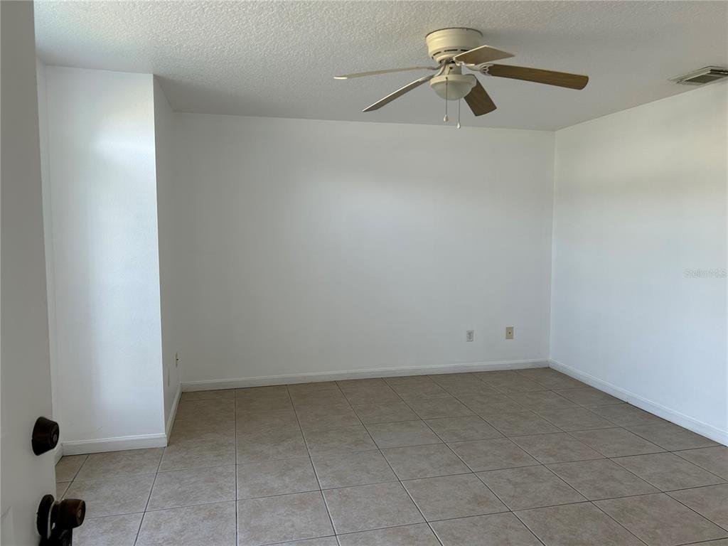 An empty room features white walls, tan tile flooring, and a ceiling fan — 3072 SHINGLE CREEK COURT, KISSIMMEE, FL