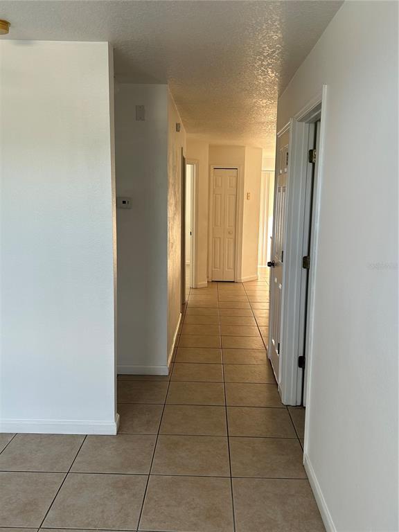A tiled hallway leads past several doorways toward a distant room with natural light — 3072 SHINGLE CREEK COURT, KISSIMMEE, FL