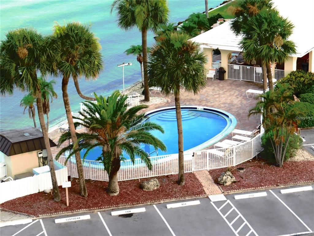 An aerial view shows a swimming pool, palm trees, and a parking lot by the water — 4550 COVE CIRCLE UNIT 106, ST PETERSBURG, FL