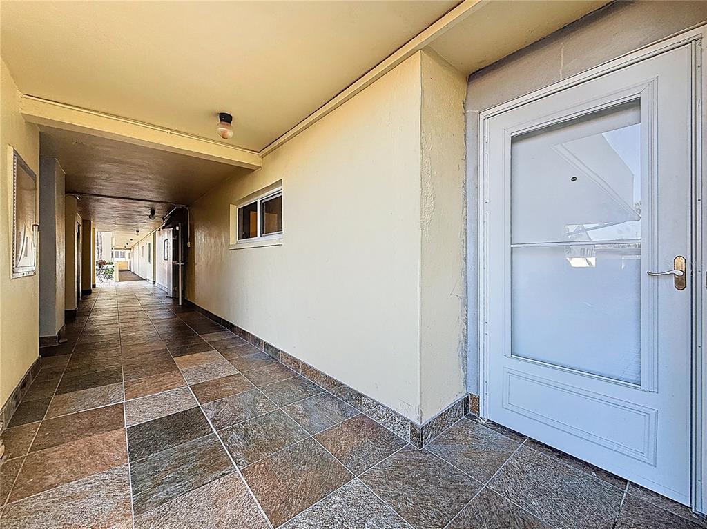 A tiled outdoor walkway leads to a white door with a glass storm door — 4550 COVE CIRCLE UNIT 106, ST PETERSBURG, FL
