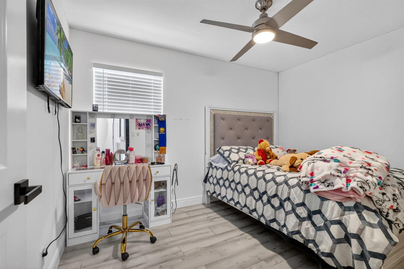 A bedroom with a bed, vanity, television, and ceiling fan on light wood-look flooring — 1691 W 26th Court, Riviera Beach FL 33404, RIVIERA BEACH, FL