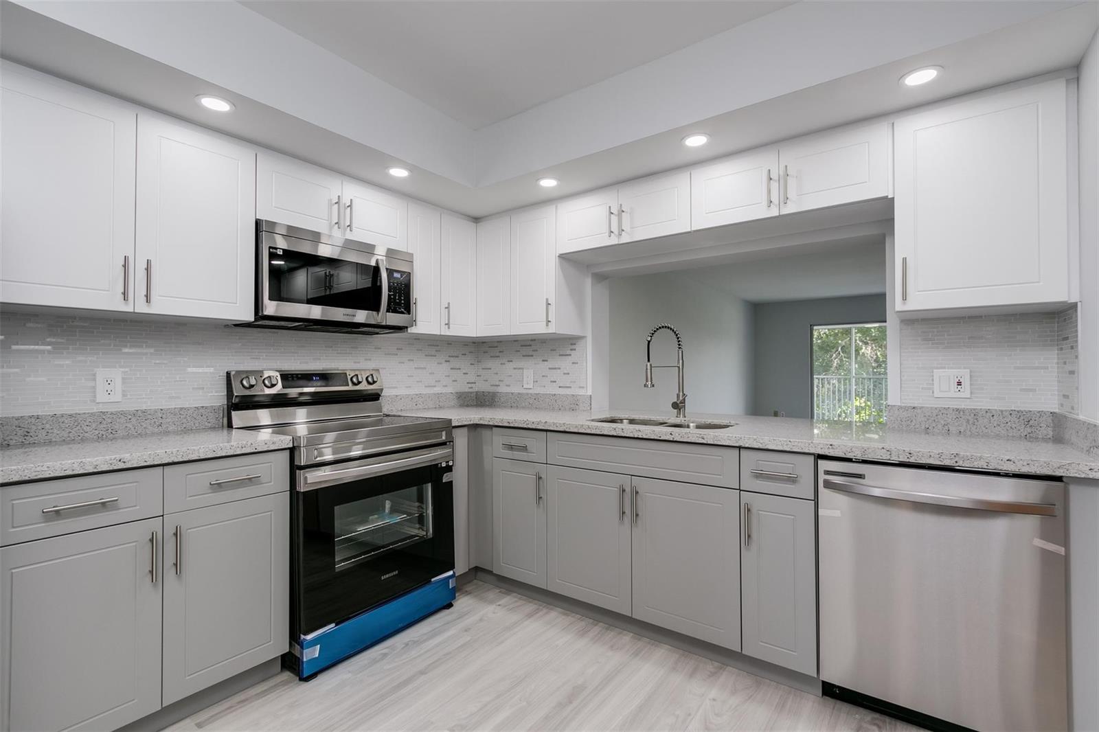 A kitchen features gray lower cabinets, white upper cabinets, stainless steel appliances, and granite countertops — 12600 SW 5th Court # 408l, Pembroke Pines FL 33027, PEMBROKE PINES, FL