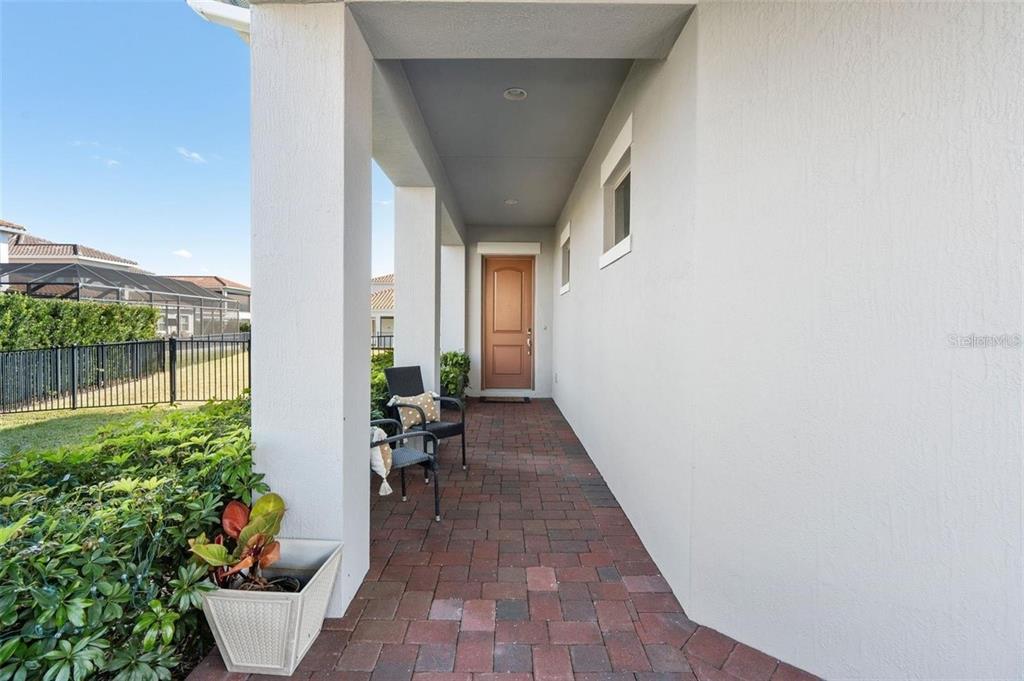A covered entryway features a brick-paved walkway, a brown front door, and two chairs — 10562 GATLEY PLACE, ORLANDO, FL