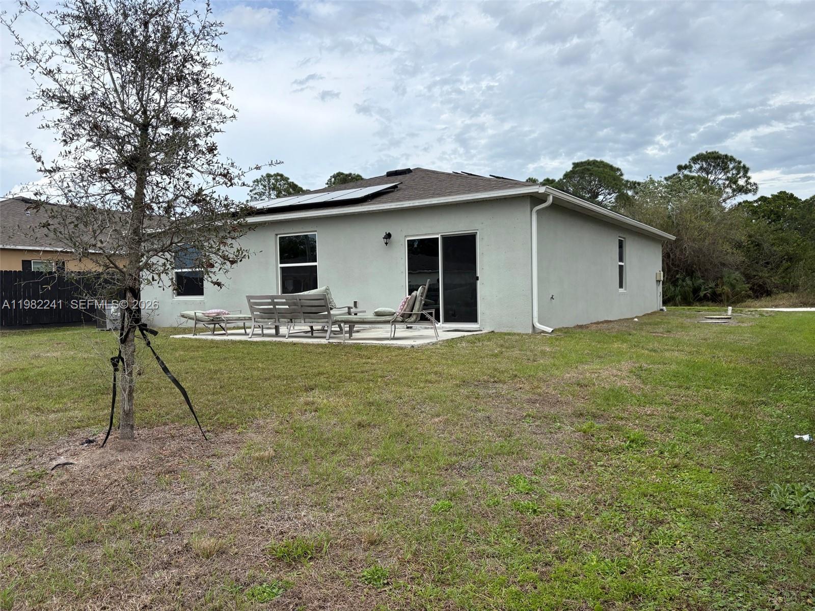 The exterior of a single-story house features a concrete patio, sliding glass doors, and solar panels — 8065 97th Ave, Vero Beach FL 32967, VERO BEACH, FL