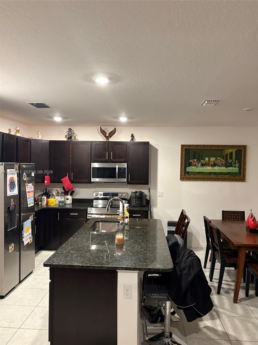 A kitchen features dark wood cabinets, granite countertops, a central island, and a dining area — 8065 97th Ave, Vero Beach FL 32967, VERO BEACH, FL