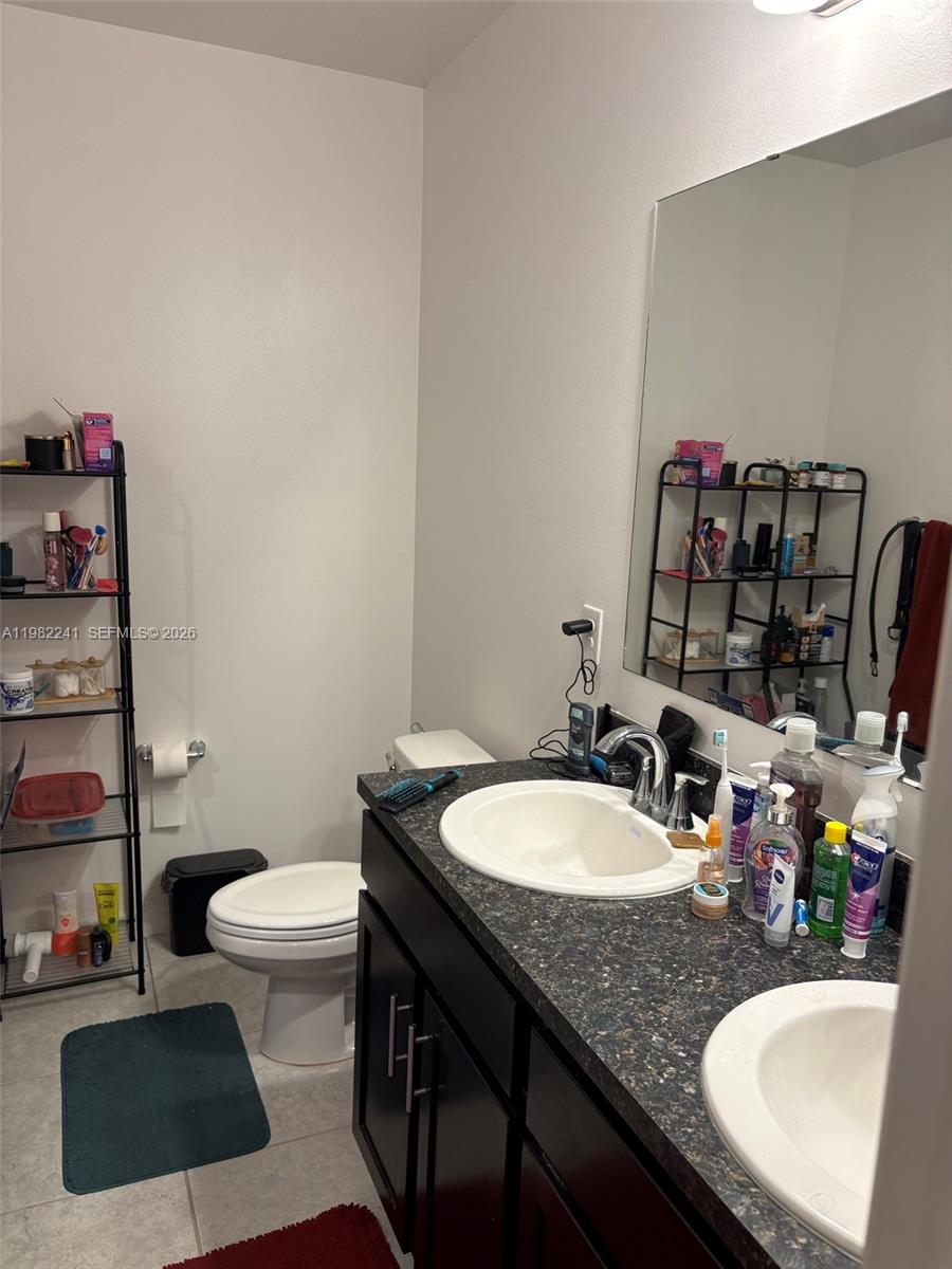 A bathroom features a dark vanity with a speckled countertop, a toilet, and metal shelving — 8065 97th Ave, Vero Beach FL 32967, VERO BEACH, FL