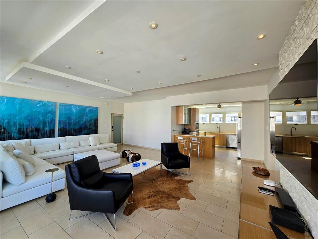 A modern open-concept living room features a white sectional, black armchairs, and a kitchen area — 1160 MAGDALENA AVENUE UNIT 7B, SAN JUAN, PR