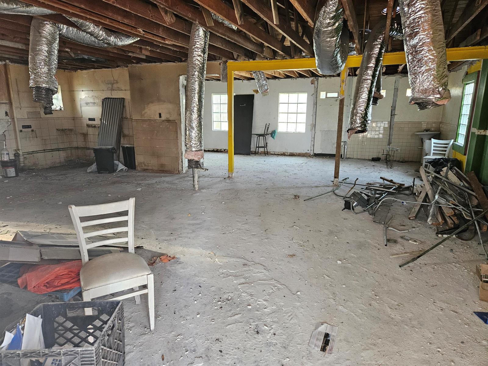 An unfinished interior space features exposed ceiling joists, hanging ductwork, and a yellow support beam — 6028 Washington Street, Hollywood FL 33023, HOLLYWOOD, FL