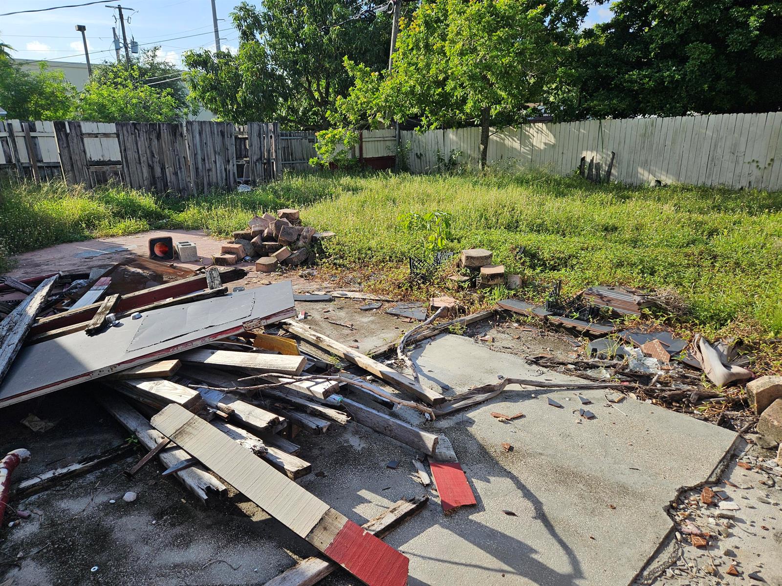A backyard area features a concrete patio covered with scattered wood debris and loose bricks — 6028 Washington Street, Hollywood FL 33023, HOLLYWOOD, FL