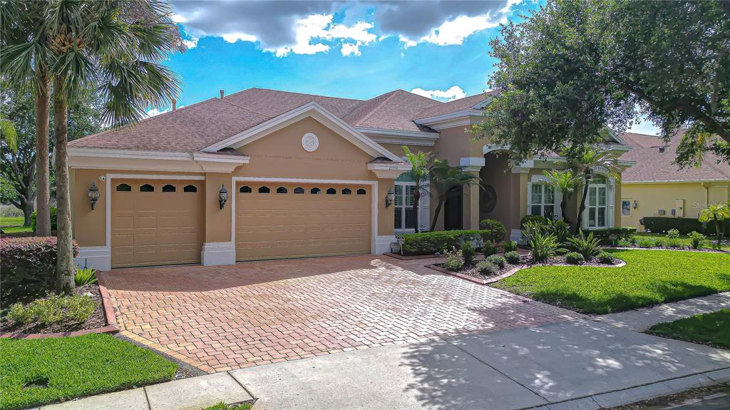 A tan single-story house with a brick paver driveway and a three-car garage — 21338 LAKE VIENNA DRIVE DRIVE, LAND O LAKES, FL