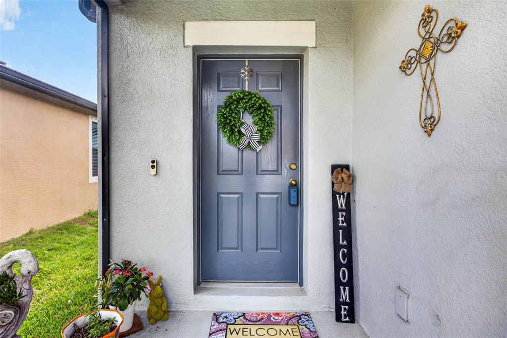 A gray front door with a wreath and welcome sign stands on a porch — 11514 LELAND GROVES DRIVE, RIVERVIEW, FL