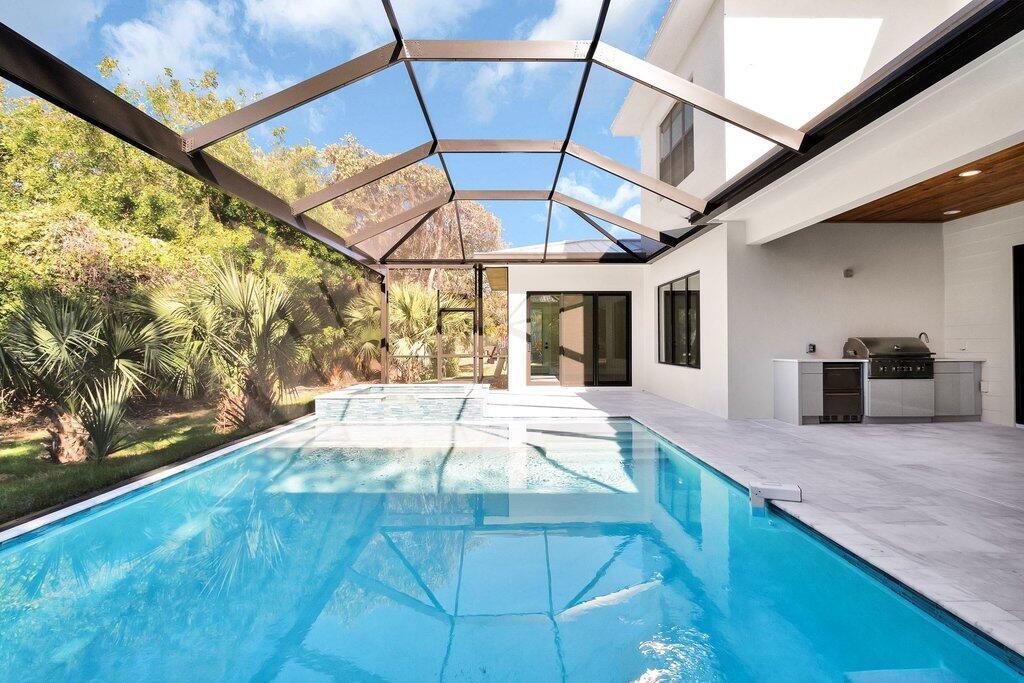A swimming pool and hot tub sit inside a screened-in patio with an outdoor kitchen — 11765 Brown Pelican Way, Vero Beach FL 32963, VERO BEACH, FL