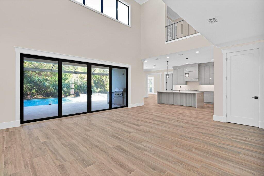 A spacious living area with light wood-look tile floors opens to a kitchen and pool — 11765 Brown Pelican Way, Vero Beach FL 32963, VERO BEACH, FL