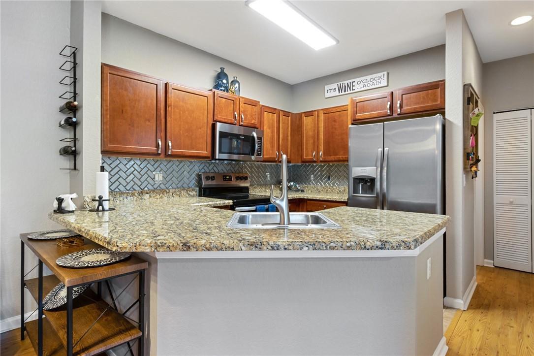 A kitchen features wood cabinets, granite countertops, stainless steel appliances, and a herringbone tile backsplash — 4809 N Wickham Circle # A, Delray Beach FL 33445, DELRAY BEACH, FL