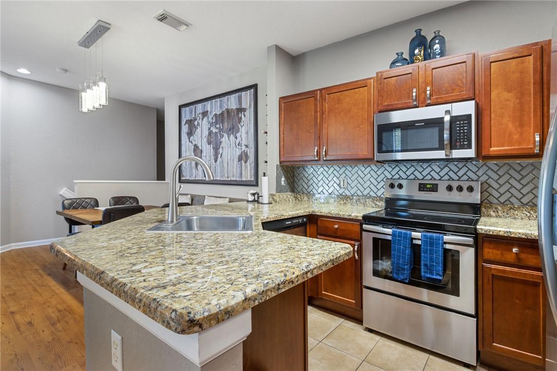 A kitchen features wood cabinets, granite countertops, stainless steel appliances, and a herringbone tile backsplash — 4809 N Wickham Circle # A, Delray Beach FL 33445, DELRAY BEACH, FL