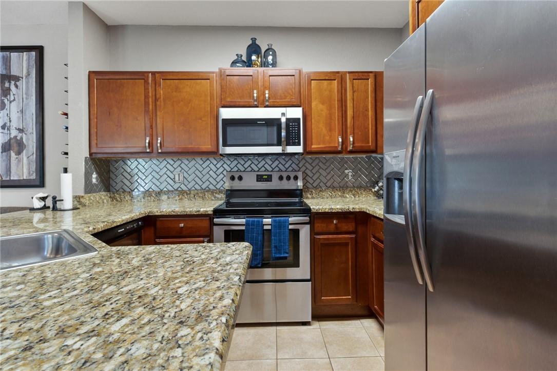 A kitchen features wood cabinets, granite countertops, stainless steel appliances, and a herringbone tile backsplash — 4809 N Wickham Circle # A, Delray Beach FL 33445, DELRAY BEACH, FL