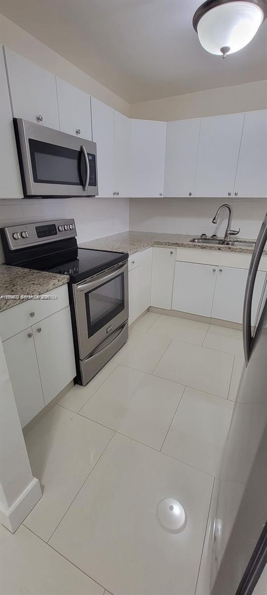 A kitchen features white cabinets, stainless steel appliances, granite countertops, and light-colored tile flooring — 6970 NW 186th St # 502, Hialeah FL 33015, HIALEAH, FL