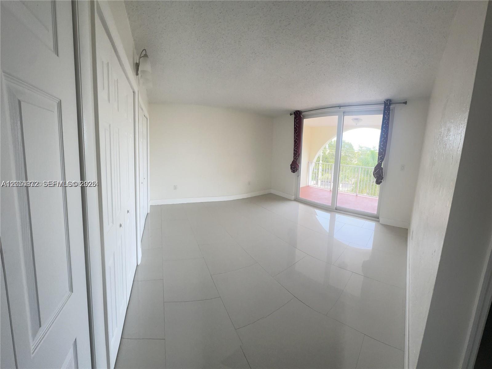 An empty room features light-colored tile flooring, white walls, closet doors, and a sliding glass door — 6970 NW 186th St # 502, Hialeah FL 33015, HIALEAH, FL