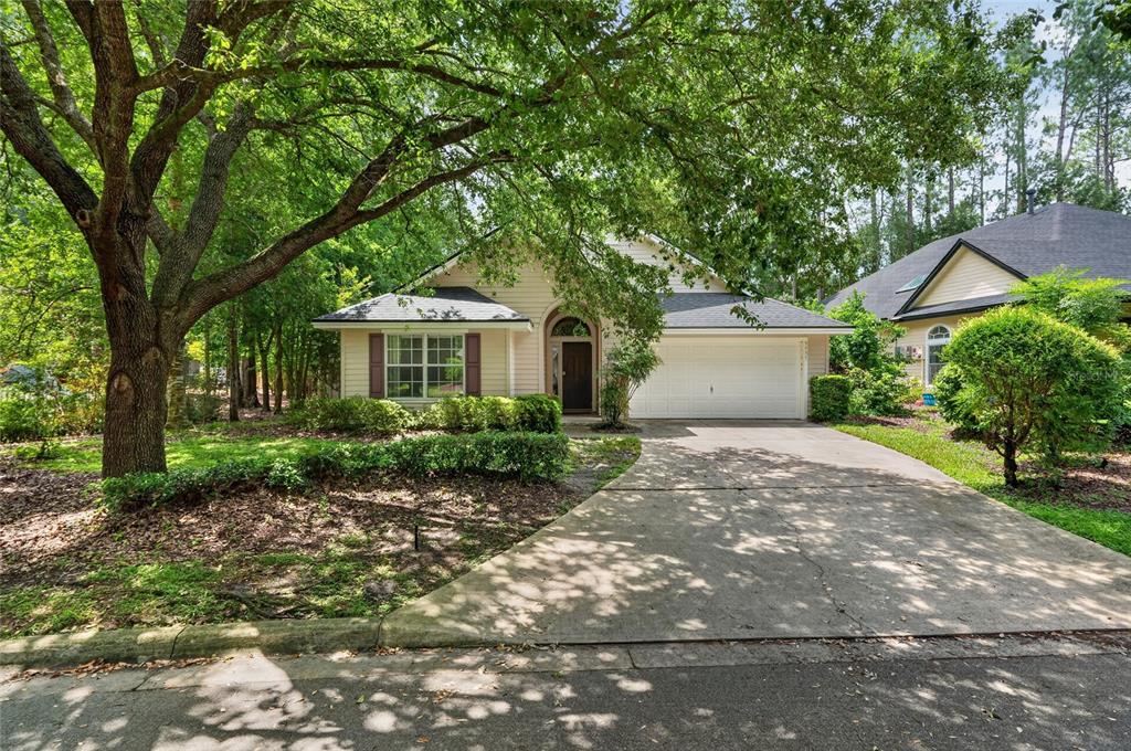A single-story house with a two-car garage, light siding, and a large tree in front — 9437 SW 31ST LANE, GAINESVILLE, FL