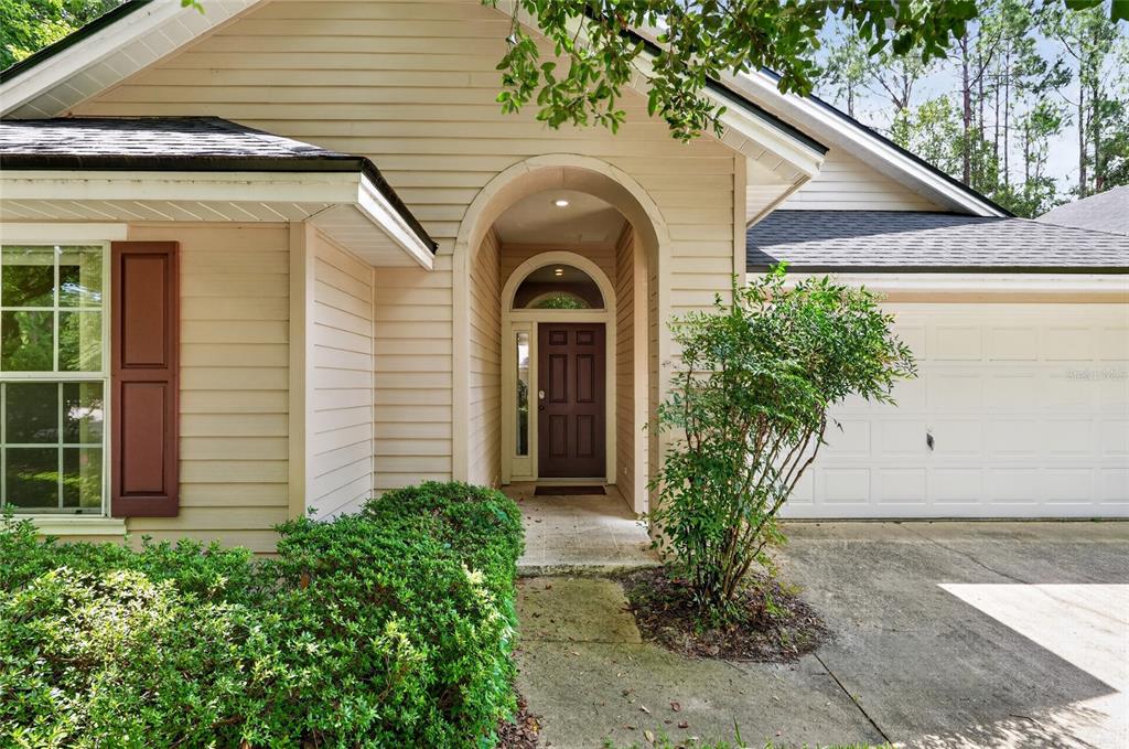 The exterior of a beige house features a dark brown front door and a garage — 9437 SW 31ST LANE, GAINESVILLE, FL