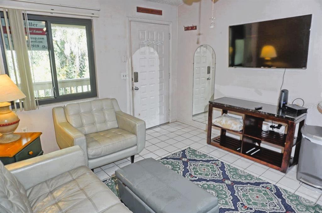 A living room features white tile floors, a gray leather armchair, and a wall-mounted television — 20893 HAULOVER COVE UNIT 8, LUTZ, FL