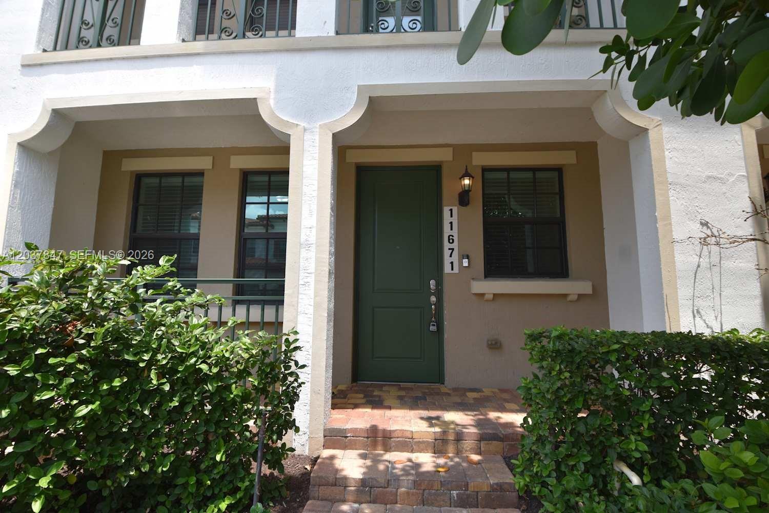 The exterior of a townhouse features a green front door, brick steps, and landscaping — PEMBROKE PINES, FL
