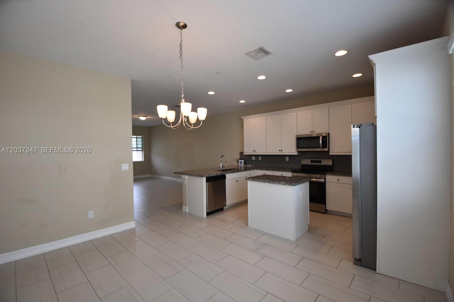 A kitchen features white cabinets, granite countertops, stainless steel appliances, and a central island — PEMBROKE PINES, FL
