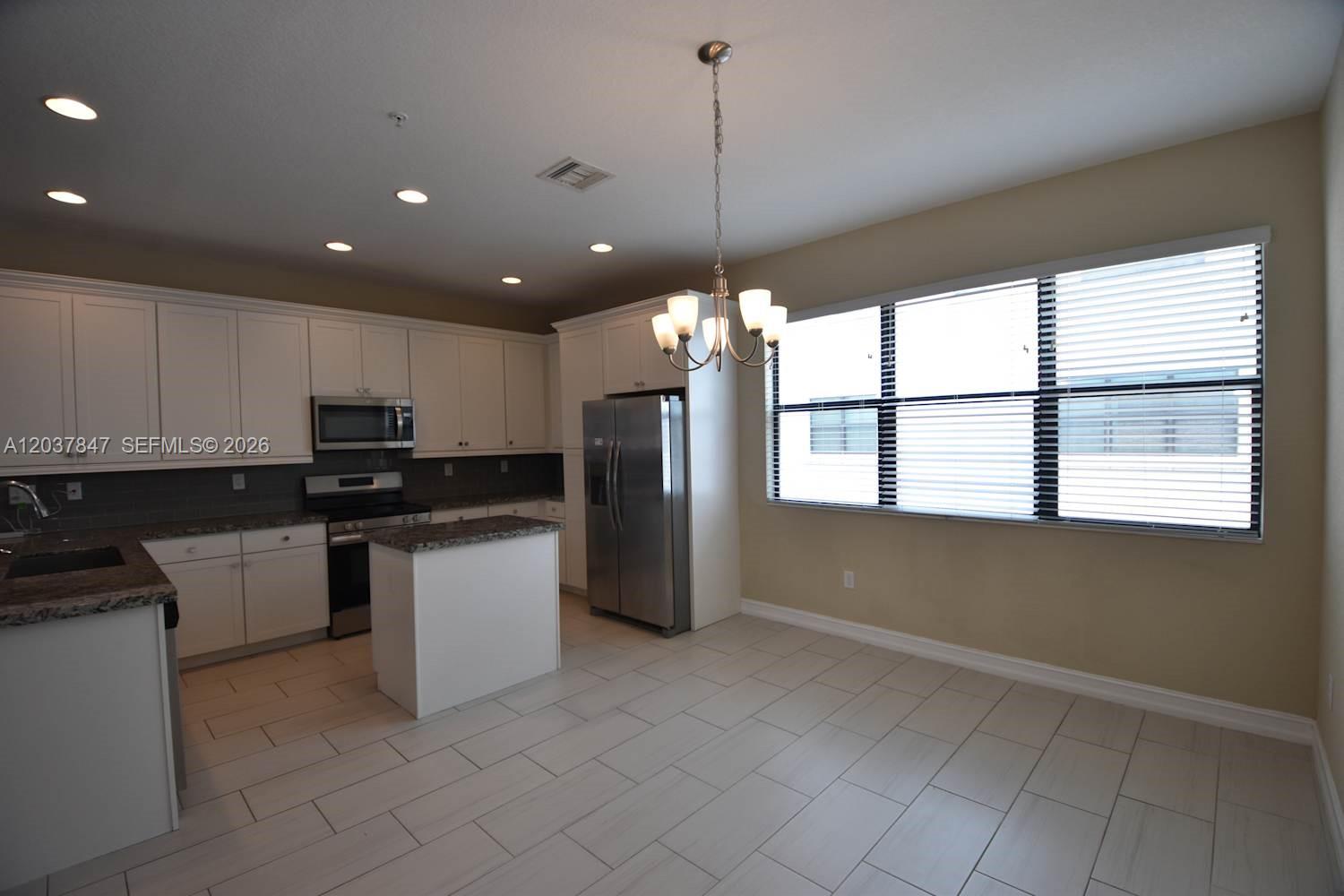A kitchen features white cabinetry, granite countertops, stainless steel appliances, and tile flooring — PEMBROKE PINES, FL