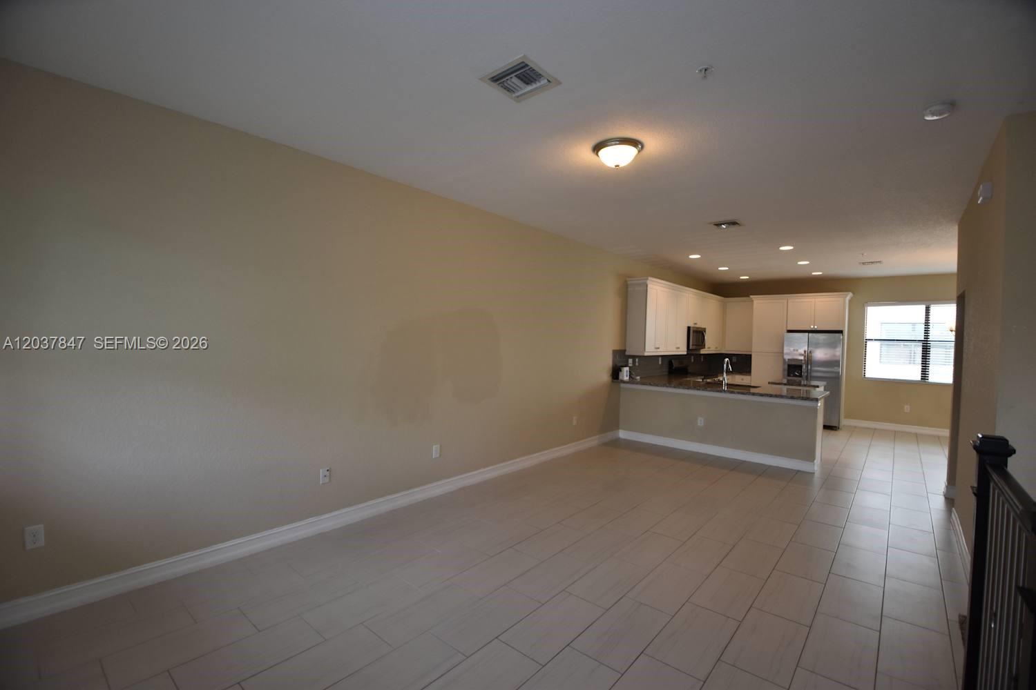 An open-concept living area features light-colored tile flooring and an adjacent kitchen with white cabinetry — PEMBROKE PINES, FL
