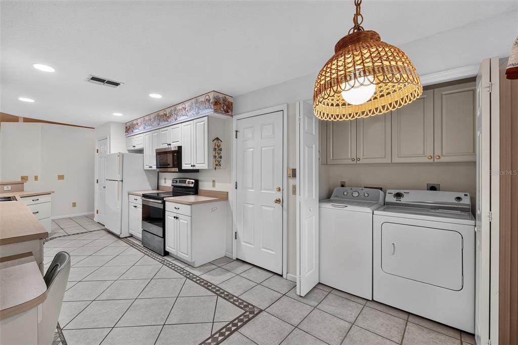 A kitchen with white cabinets, tile flooring, and a laundry area with a wicker pendant light — 110 MORNING GLORY CIRCLE, WINTER HAVEN, FL