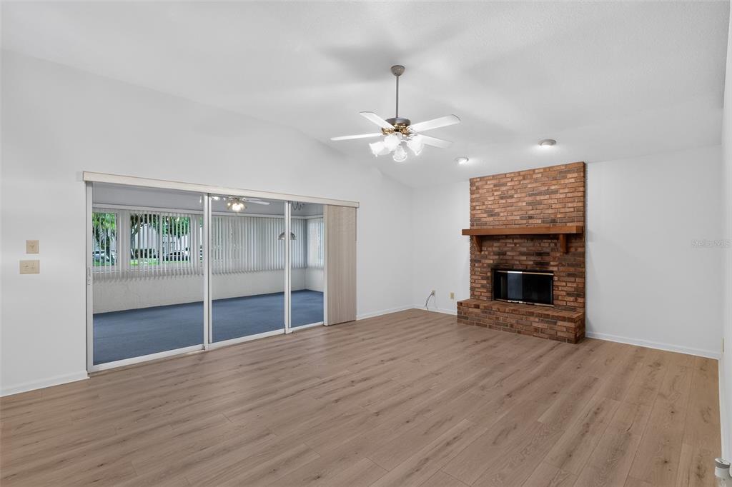 A living room with light wood flooring, a brick fireplace, and sliding glass doors — 110 MORNING GLORY CIRCLE, WINTER HAVEN, FL
