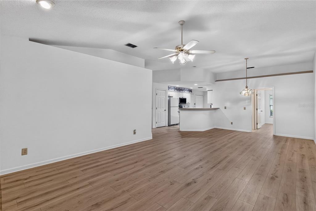 An open-concept living area features light wood-look flooring, white walls, and a ceiling fan — 110 MORNING GLORY CIRCLE, WINTER HAVEN, FL