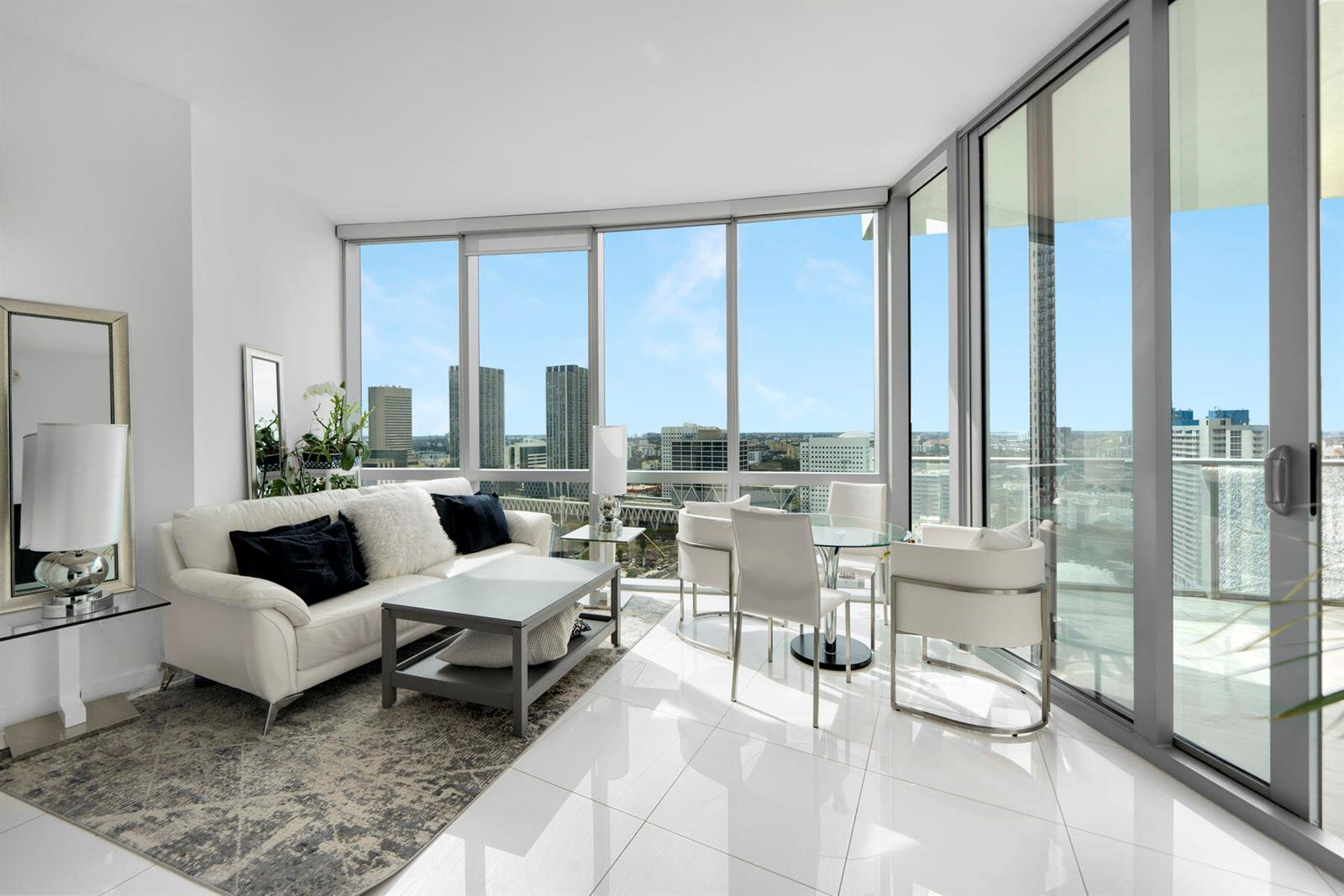 A modern living room with white tile floors, a white sofa, and floor-to-ceiling city views — 851 NE 1st Avenue # 2410, Miami FL 33132, MIAMI, FL