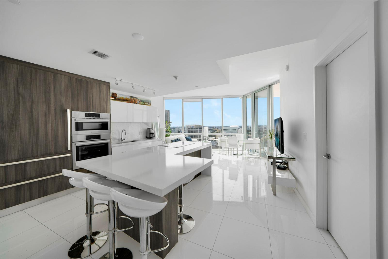 A modern kitchen with white countertops, dark wood cabinetry, and floor-to-ceiling windows overlooking a city — 851 NE 1st Avenue # 2410, Miami FL 33132, MIAMI, FL