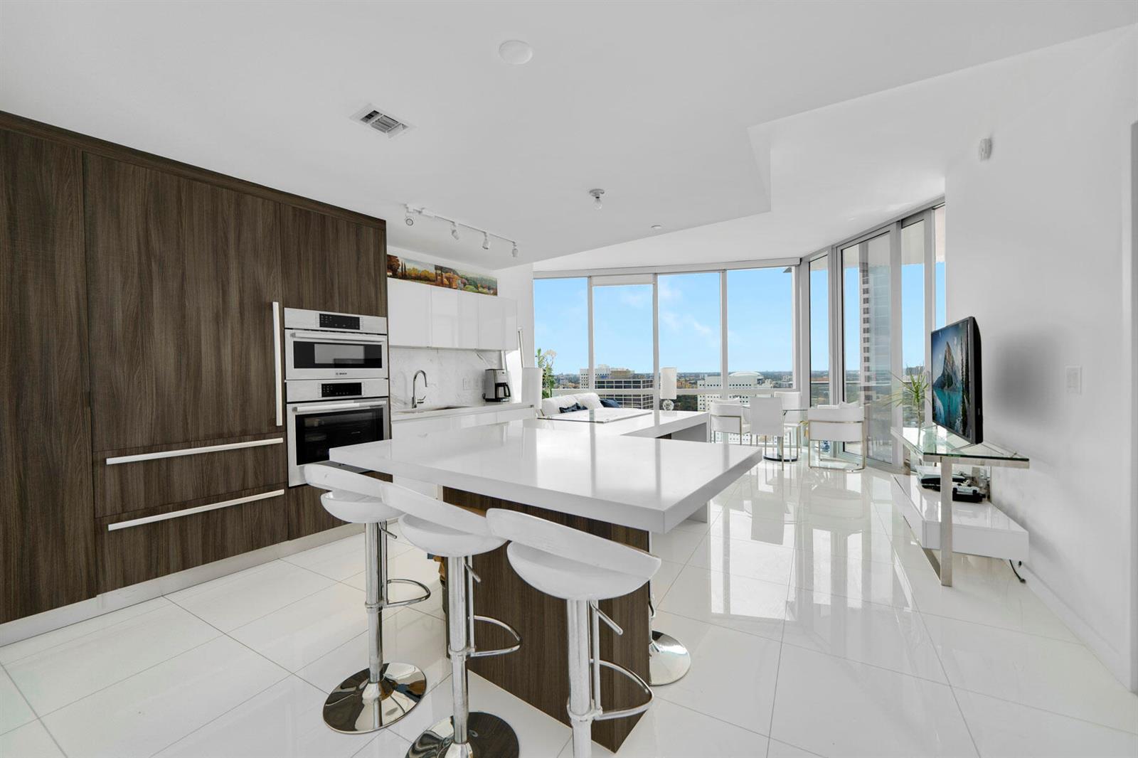 A modern kitchen features white countertops, dark wood cabinetry, and bar stools on white tile floors — 851 NE 1st Avenue # 2410, Miami FL 33132, MIAMI, FL