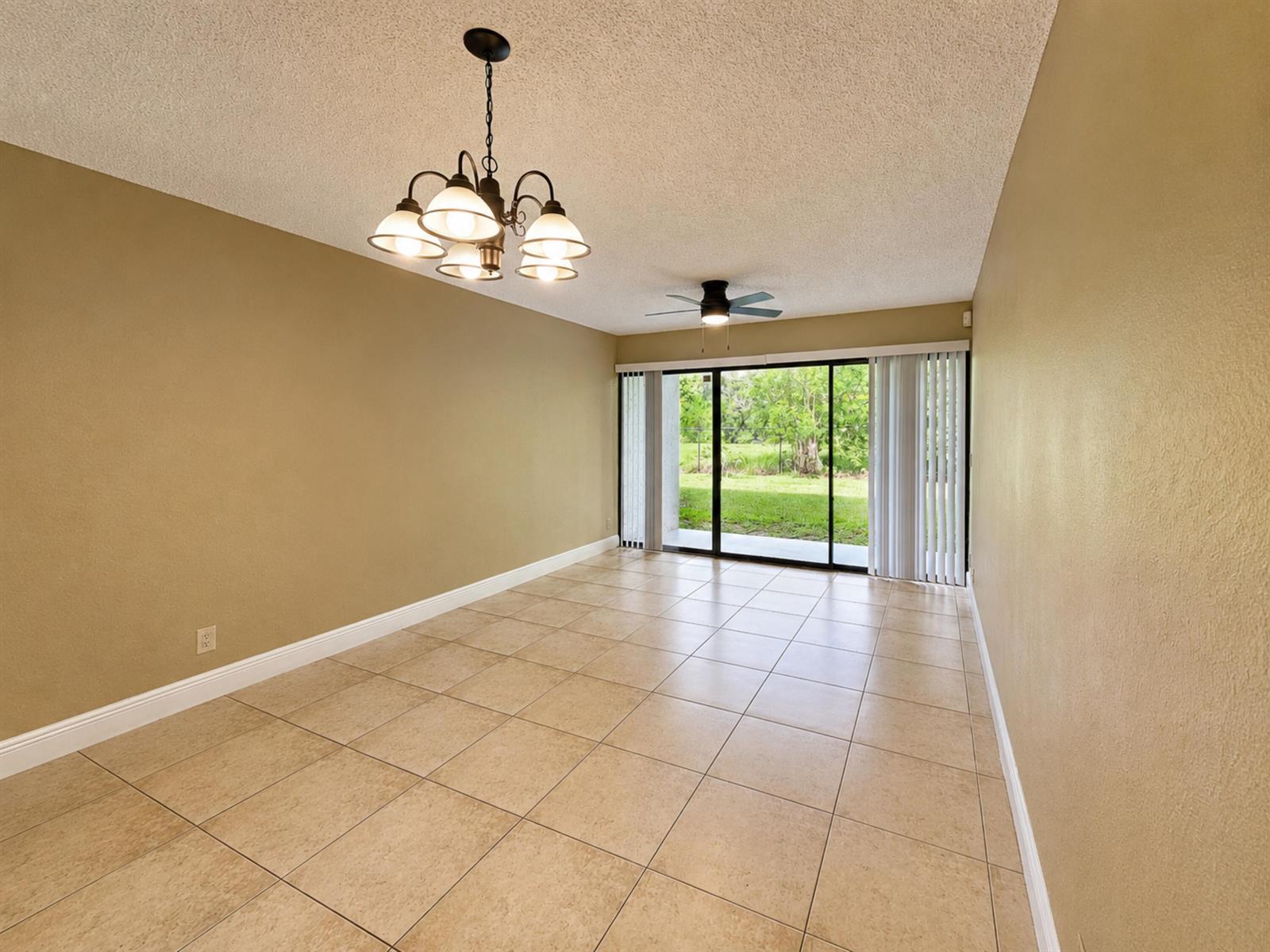 An empty dining room features tan walls, tile flooring, a chandelier, and sliding glass doors — 1461 Windorah Way # C, West Palm Beach FL 33411, WEST PALM BEACH, FL