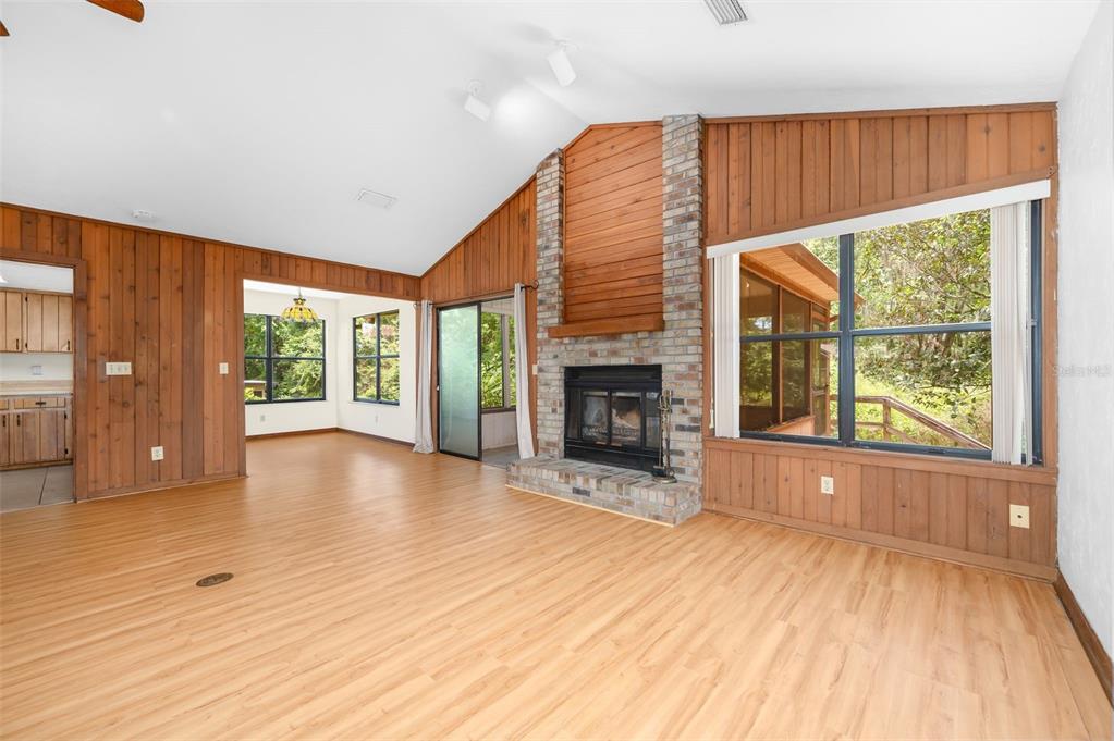 A living room with wood-paneled walls, a brick fireplace, and light-colored wood flooring — 1301 NW 94TH STREET, GAINESVILLE, FL