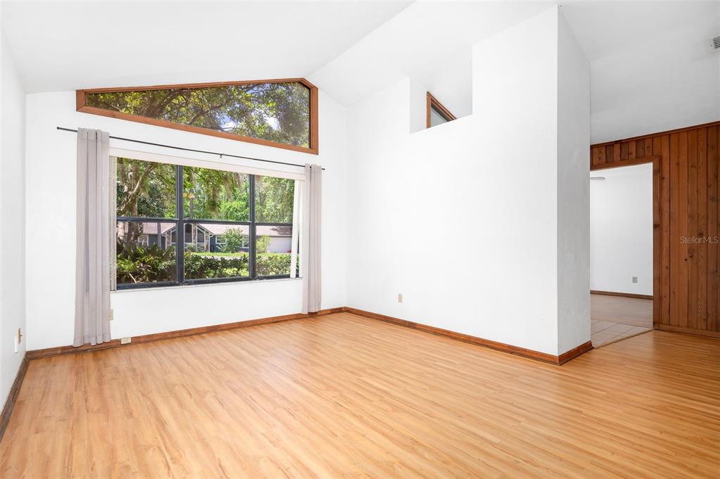 An empty living room features light wood flooring, white walls, and a large window — 1301 NW 94TH STREET, GAINESVILLE, FL