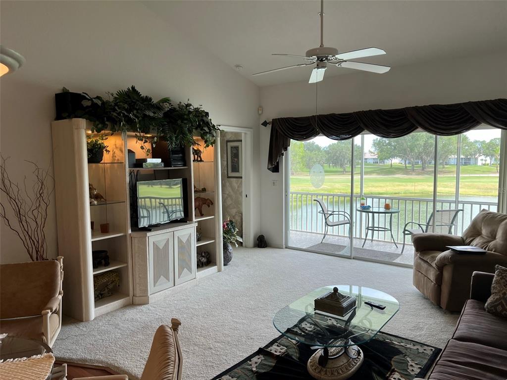 A living room features a large entertainment center, a ceiling fan, and sliding glass doors — 6632 PINEVIEW TERRACE UNIT 10-201, BRADENTON, FL