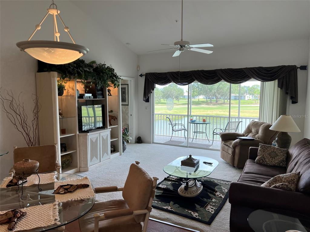A living room with a glass-topped coffee table, brown sofa, and sliding doors overlooking a pond — 6632 PINEVIEW TERRACE UNIT 10-201, BRADENTON, FL